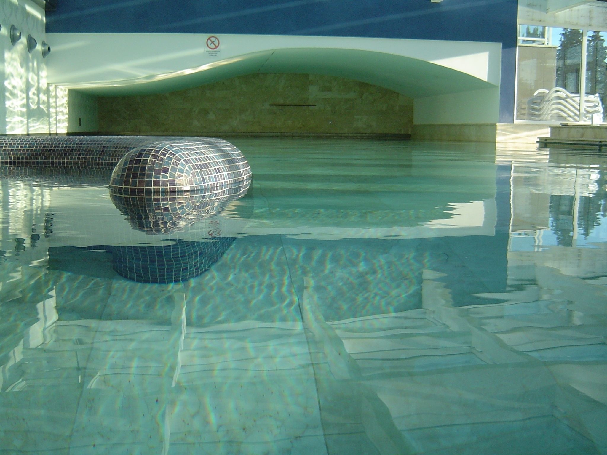Una piscina con un objeto esférico, agua cristalina y un letrero de prohibido bañarse.