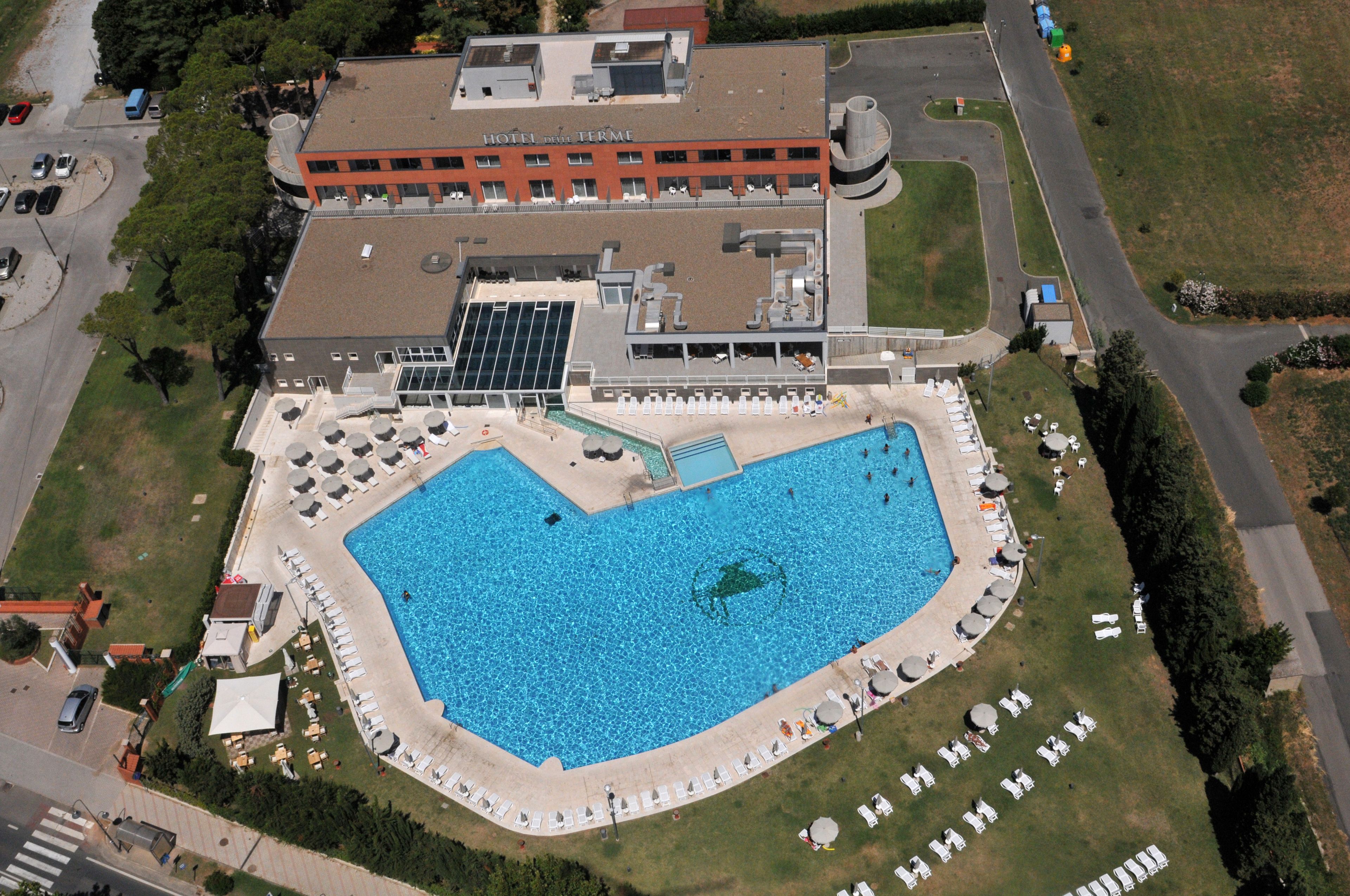Vue aérienne d’un hôtel doté d’une grande piscine, de chaises longues et d’un espace abrité avec des parasols.