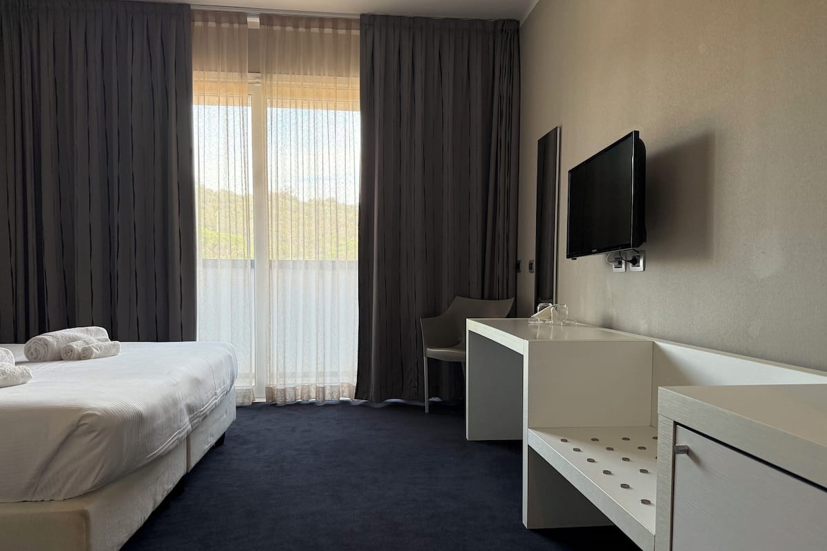 Ein Hotelzimmer mit Bett, Schreibtisch, Stuhl, Fernseher und einem Fenster mit Vorhängen.