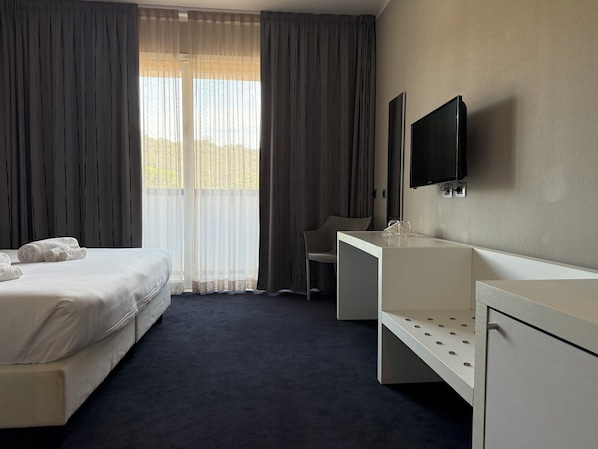 Habitación de hotel con cama, escritorio, silla, televisor y ventana con cortinas.