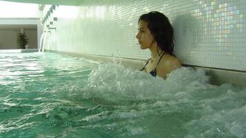 Una persona en un jacuzzi con una pared de azulejos y una escalera al fondo.
