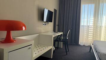 Ett hotellrum med ett skrivbord, en stol, en säng, en TV och ett fönster med gardiner.