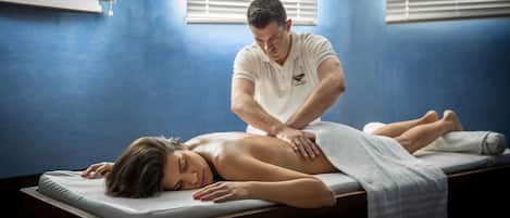 En massagebehandling i et rum med blå vægge og et vindue med skodder.