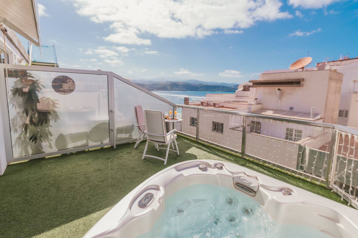 A balcony with a hot tub, a chair, and a table with a drink.