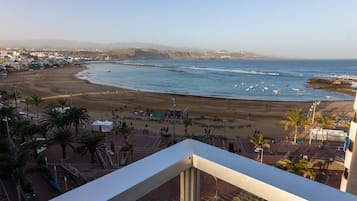 Uitzicht op de kust vanaf een balkon, met een strand, palmbomen, een zandstrand en boten in het water.