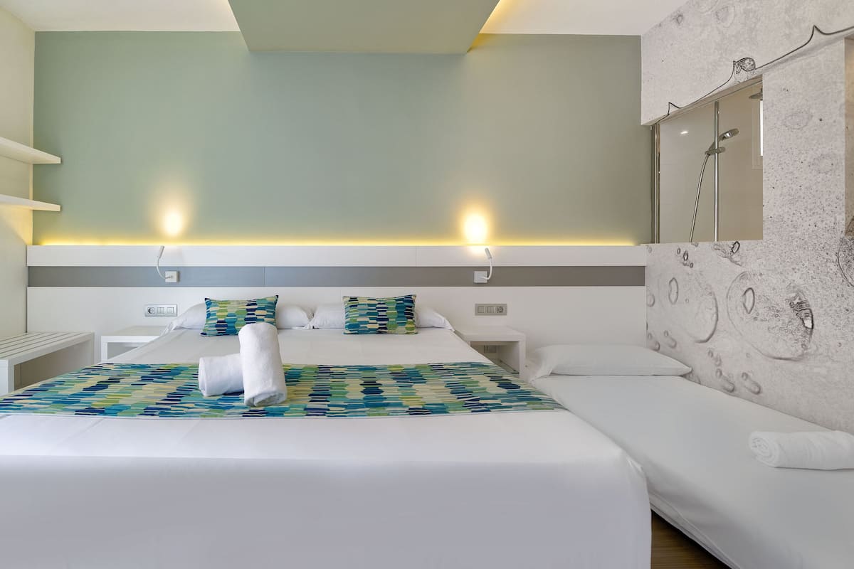 A modern hotel room with a large bed, a bedside table, a bench, and a shower area.