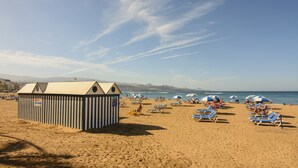 A beach with striped beach huts, sun loungers, and umbrellas. - Hotel Aloe Canteras (Las Palmas de Gran Canaria)