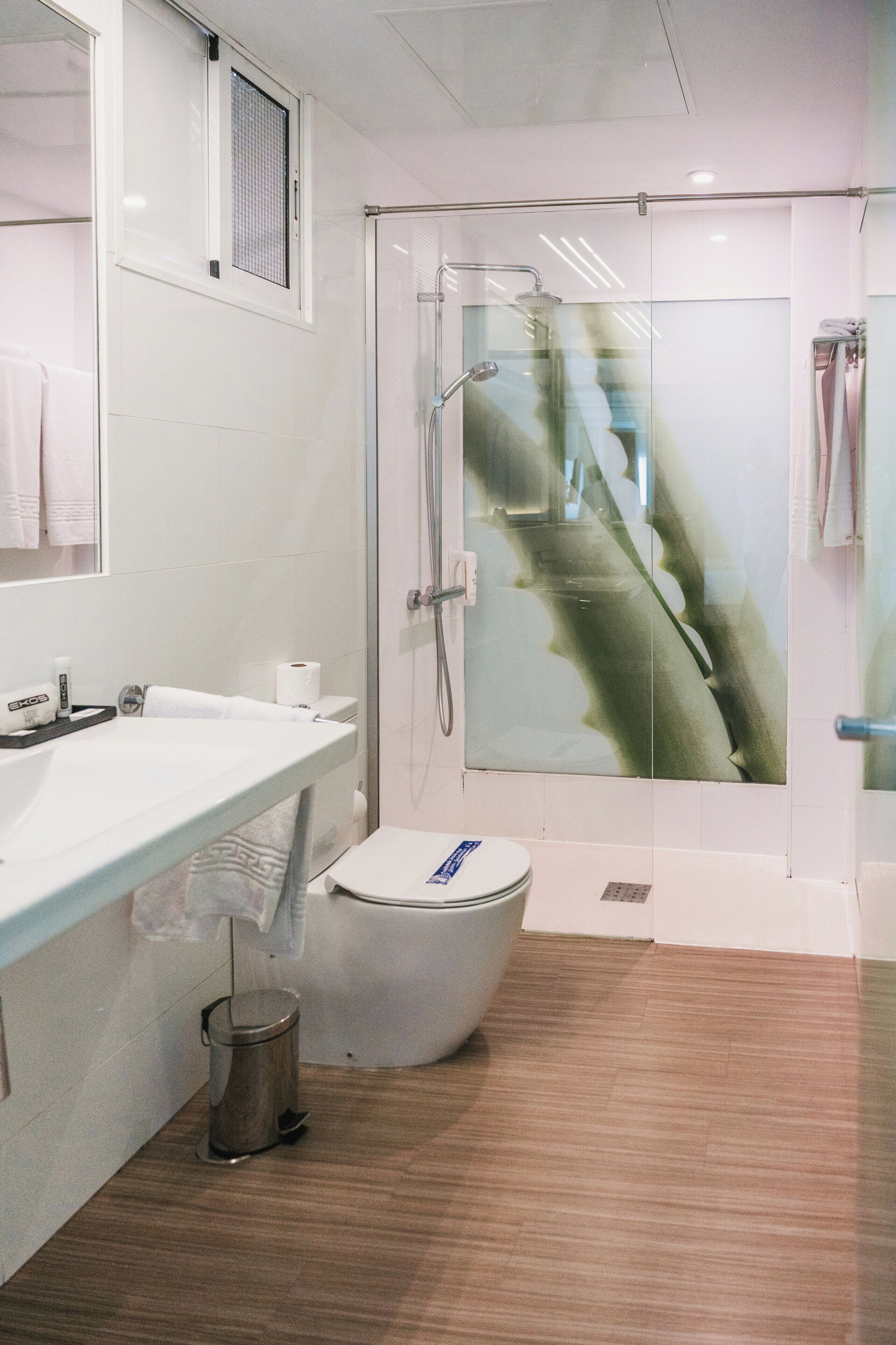 A modern bathroom with a glass shower enclosure, a toilet, and a sink with a trash can.