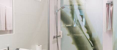 A modern bathroom with a glass shower enclosure, a toilet, and a sink with a trash can.