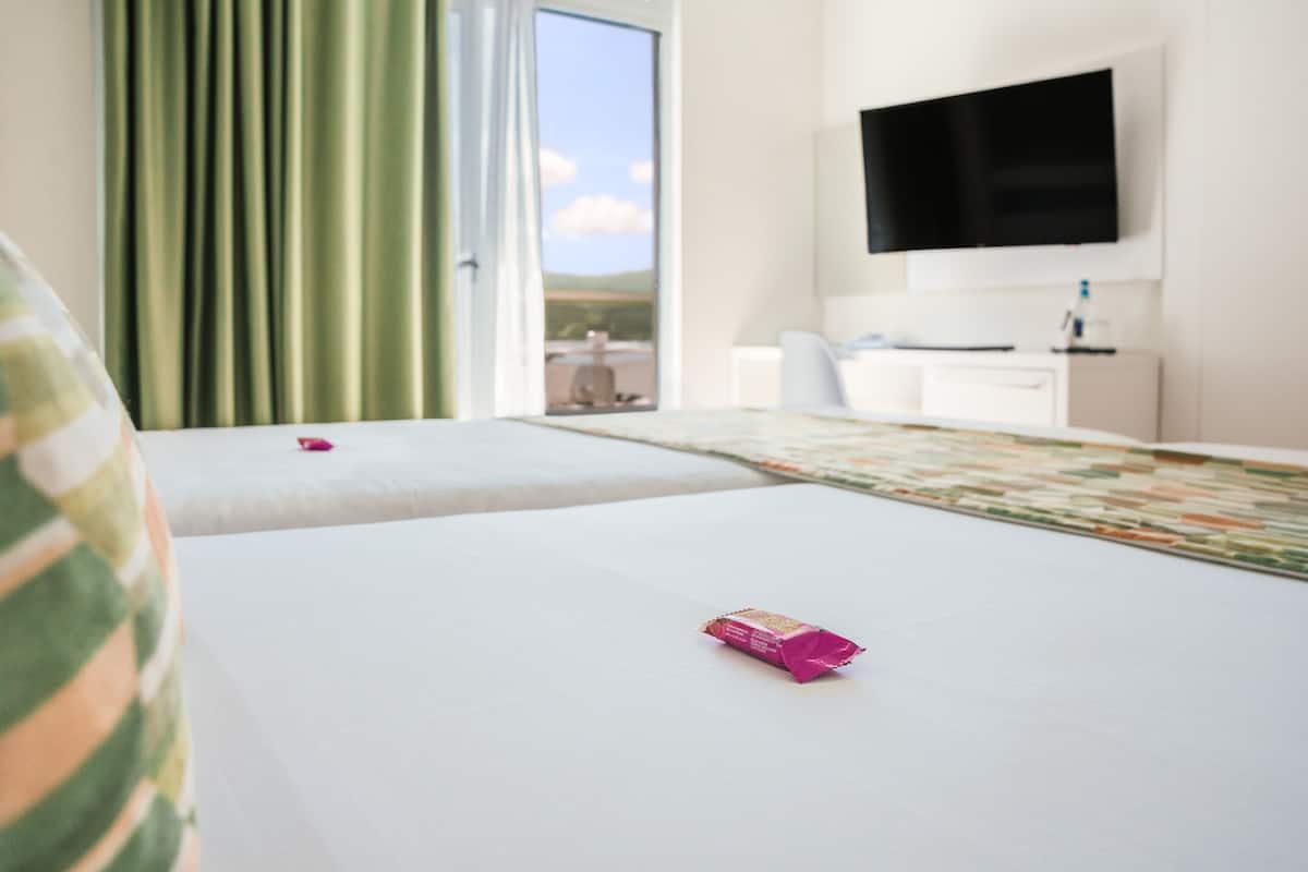 A hotel room with two beds, a flat-screen TV, a desk, and a view of the outdoors.