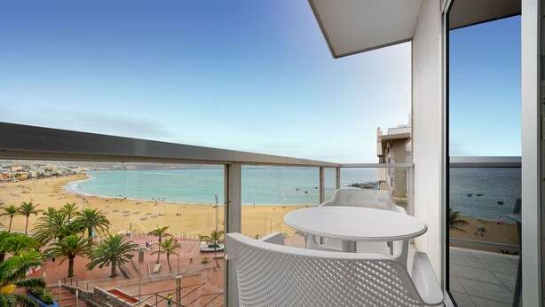 A balcony with a view of a beach, a white table, and chairs. - Hotel Aloe Canteras (Las Palmas de Gran Canaria)