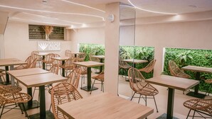 A modern hotel dining area with wicker chairs and light wood tables, a green wall with plants, and a sign for Hotel ALOE Canteras. - Hotel Aloe Canteras (Las Palmas de Gran Canaria)