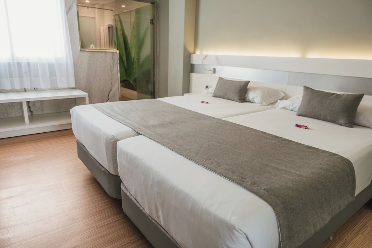 A double bed with a grey blanket, a bedside table, and a mirror.
