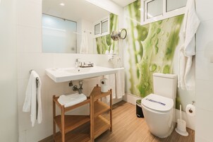 A modern bathroom with a white sink, wooden chair, and a toilet.