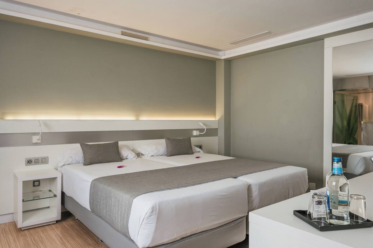 A hotel room with a bed, bedside tables, a mirror, and a tray with toiletries.
