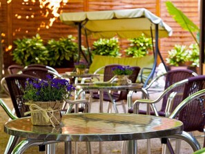 An outdoor patio area with round tables and chairs, some with potted plants and flowers.