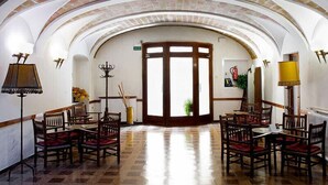 Un hall spacieux et bien éclairé, doté d’un plafond haut et d’une structure en briques en forme d’arc. On y trouve plusieurs tables et chaises en bois, disposées pour accueillir les visiteurs.