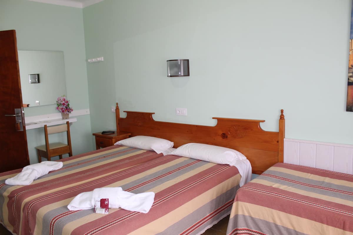 Hotelkamer met twee bedden, een houten hoofdbord, nachtkastje, spiegel en een tafeltje met een bloevas.