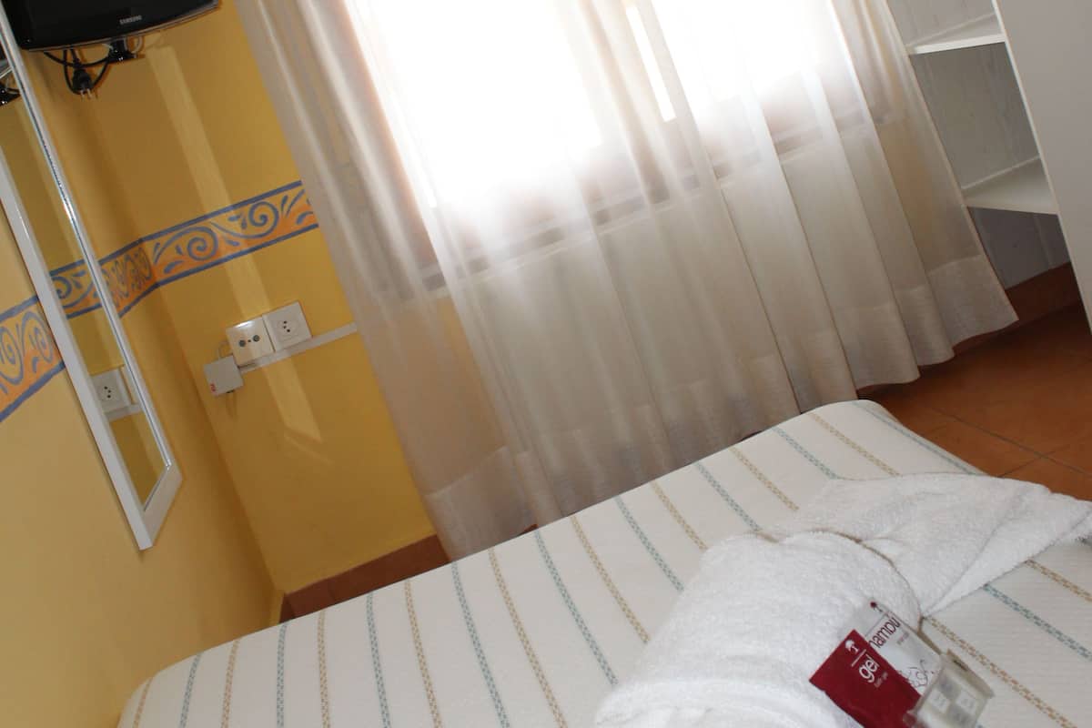 Een hotelkamer met een bed, een aan de muur bevestigde televisie en een raam met dunne gordijnen.