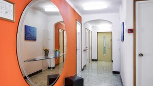 Un couloir avec un grand miroir, une étagère en verre ornée de fleurs et un banc noir.