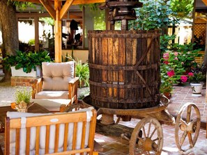 A rustic outdoor seating area with a wooden barrel and wheels, surrounded by potted plants and a cushioned chair.