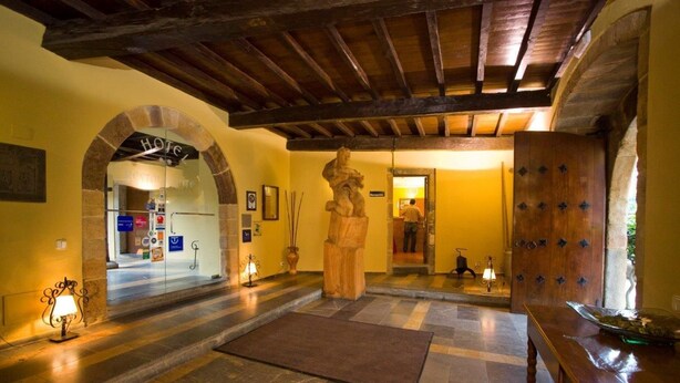 Un hall d’hôtel agrémenté d’une arche en pierre, d’une statue en bois, d’une porte en bois ornée de clous métalliques décoratifs et d’un comptoir d’accueil.
