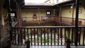 Une cour avec un balcon en bois, des plantes en pot et un sol carrelé.