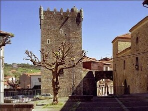 A stone tower with battlements, a tree in front, and a building with a tiled roof. - Hotel Castillo de Valdés Salas (Salas)