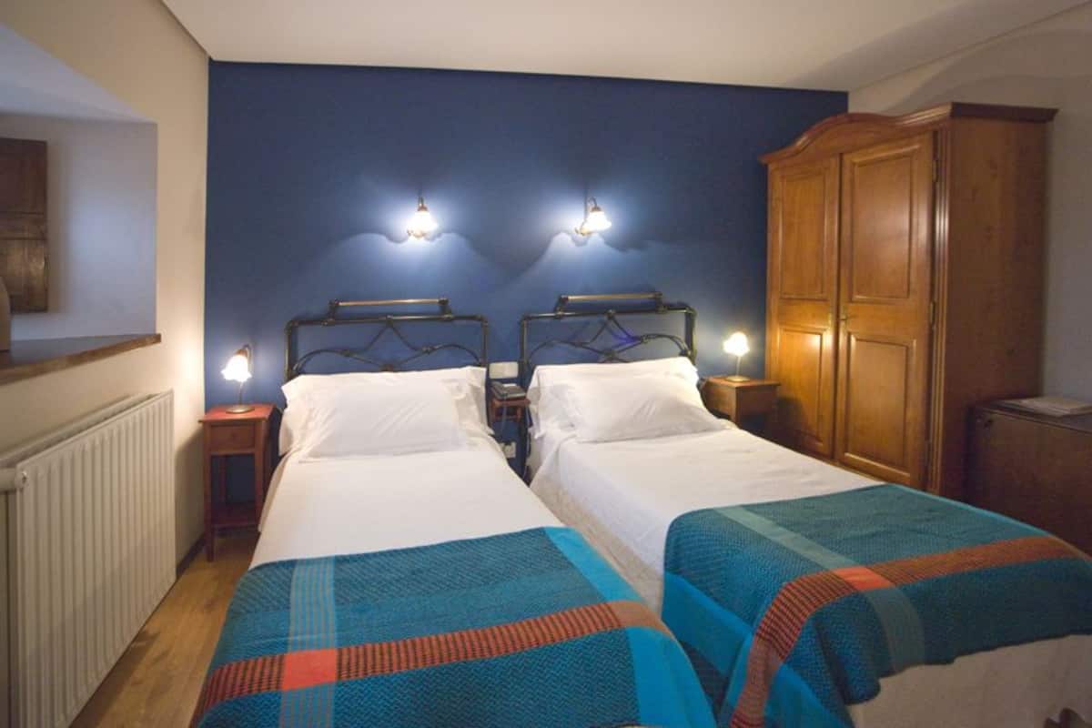 A double room with two beds, each with a headboard, bedside tables, and lamps. There is a wooden wardrobe and a radiator on the wall.