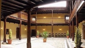 Une cour spacieuse avec un balcon en bois, des plantes en pot et un sol carrelé.