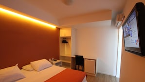 A hotel room with a bed, a desk, a chair, a small fridge, and a wall-mounted TV. - Hotel Don Zepe (Florianópolis)