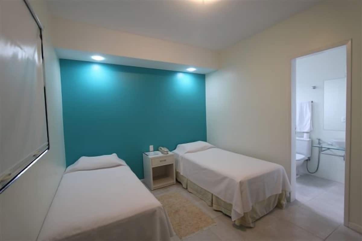 A small, clean room with two beds, a nightstand, and a bathroom visible through an open door.