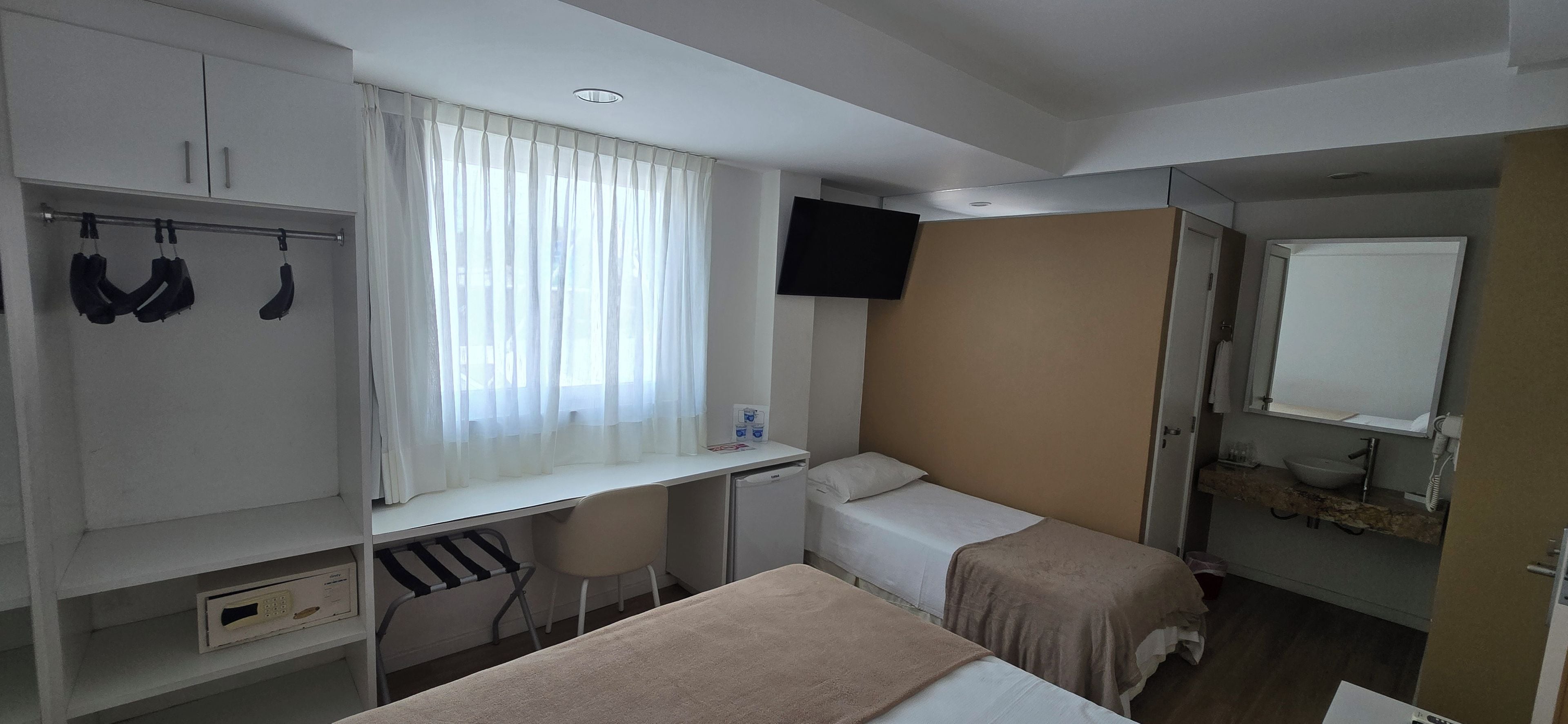 Una habitación de hotel con cama, escritorio, televisor, armario y baño.