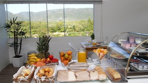 A breakfast buffet with various fruits, bread, and pastries, set against a backdrop of a scenic mountain view. - Hotel Don Zepe (Florianópolis)