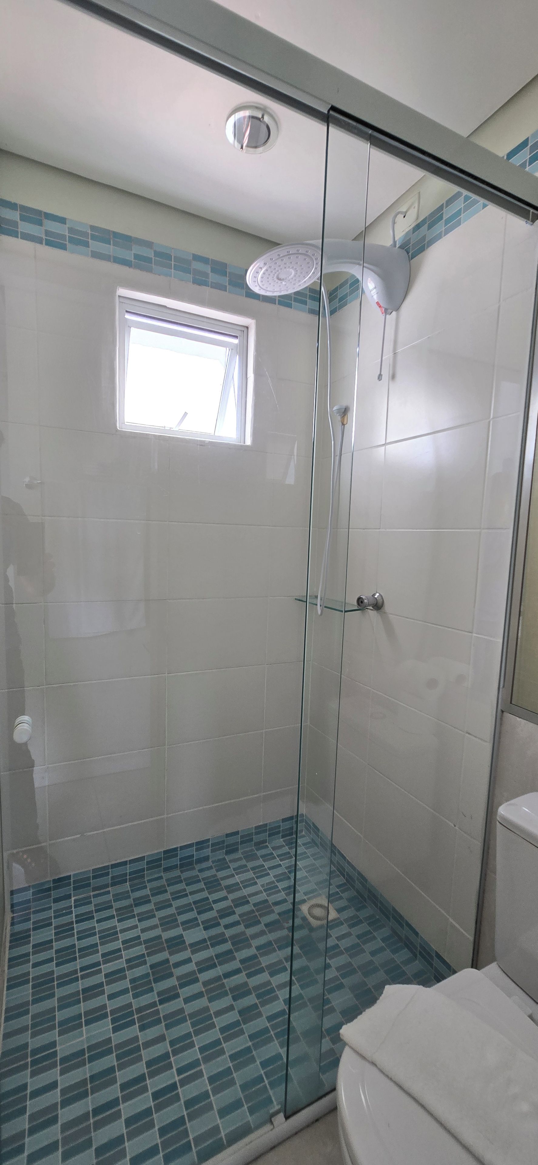 A glass-enclosed shower with a tiled floor and a small window.