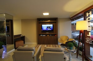 A hotel room with a TV, seating area, and a lamp.