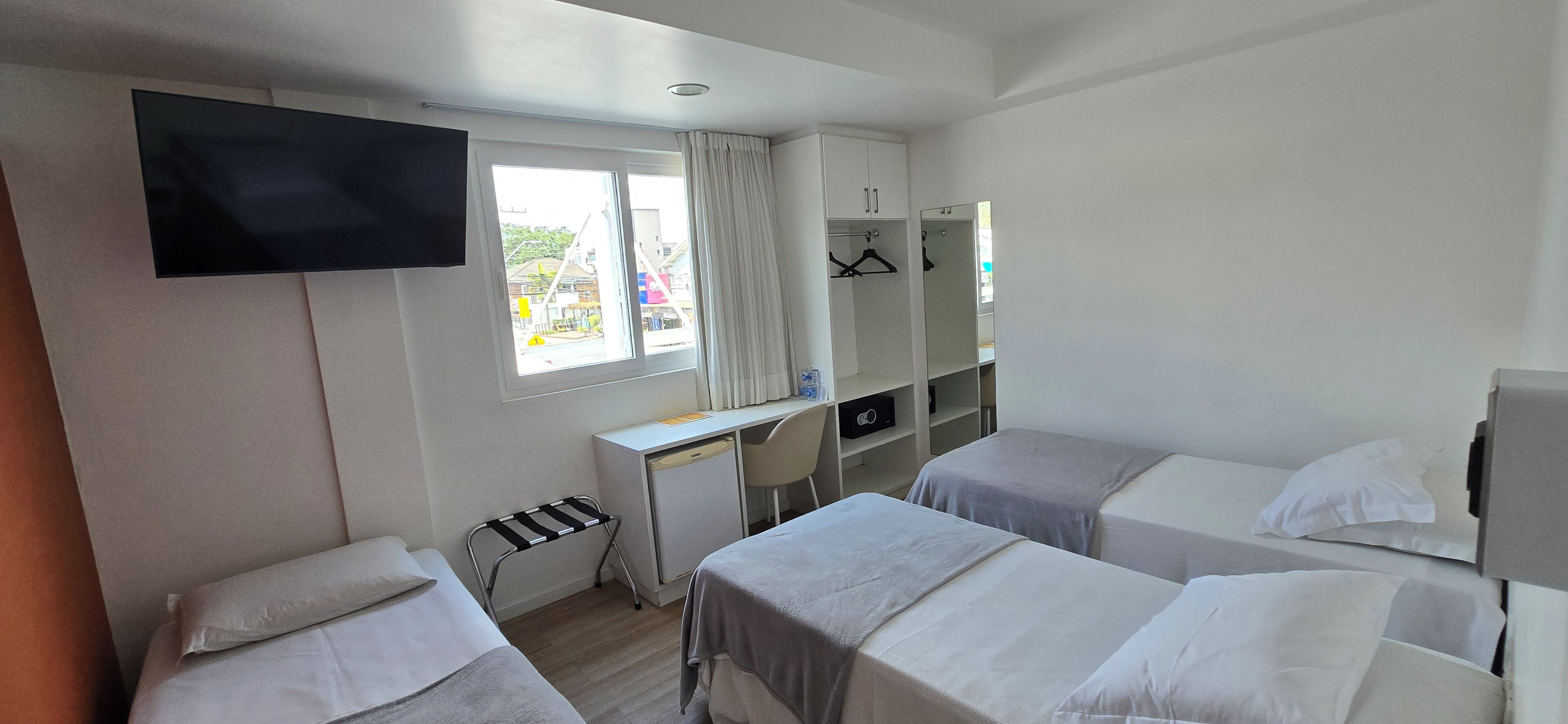 Een hotelkamer met twee bedden, een bureau, een televisie en een raam met gordijnen.