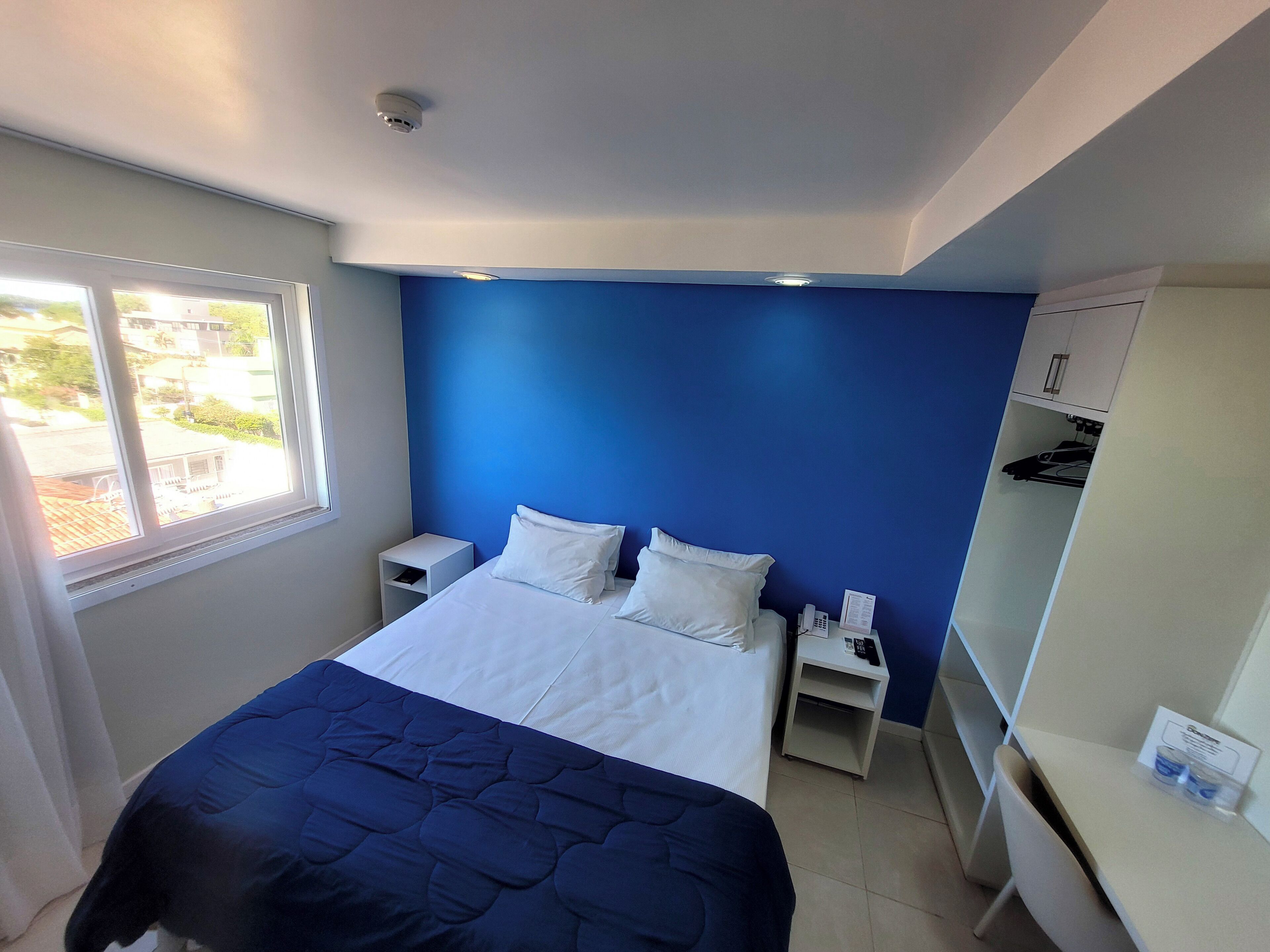 A bedroom with a bed, a nightstand, a desk, and a wardrobe.