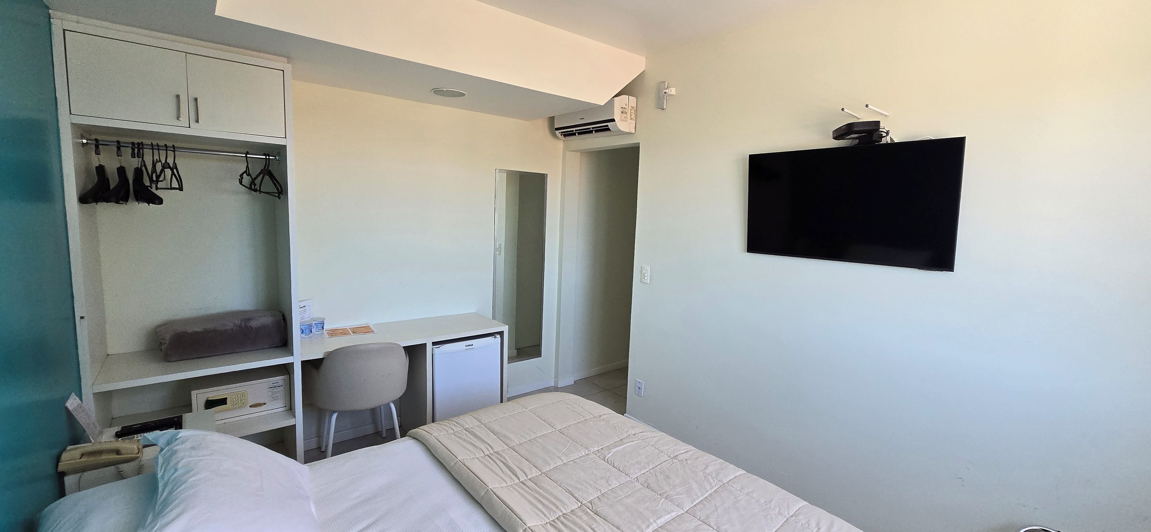 A bedroom with a bed, a desk, a chair, a wardrobe, and a TV mounted on the wall.