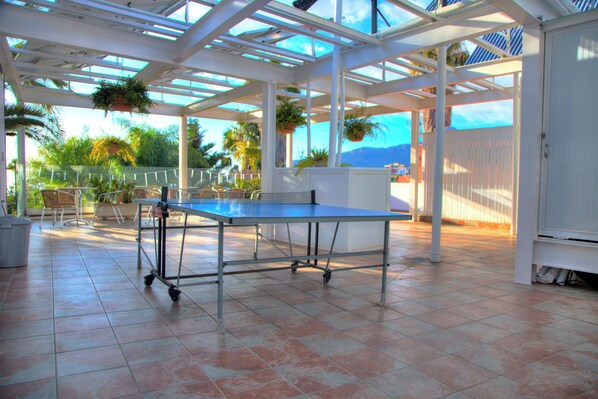A covered patio area with a ping pong table, chairs, and potted plants. - Adjovimar Apartamentos (Los Llanos de Aridane)