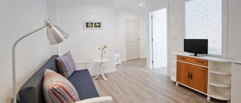 A modern room with a sofa, a small table, a lamp, a TV, and a cabinet.