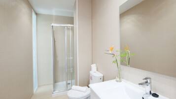 A modern bathroom with a glass shower enclosure, a white toilet, and a sink with a mirror.