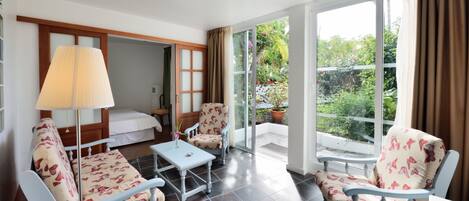 Habitación de hotel con cama, dos sillas, una mesa, lámpara y un ventanal que ofrece vistas al jardín.