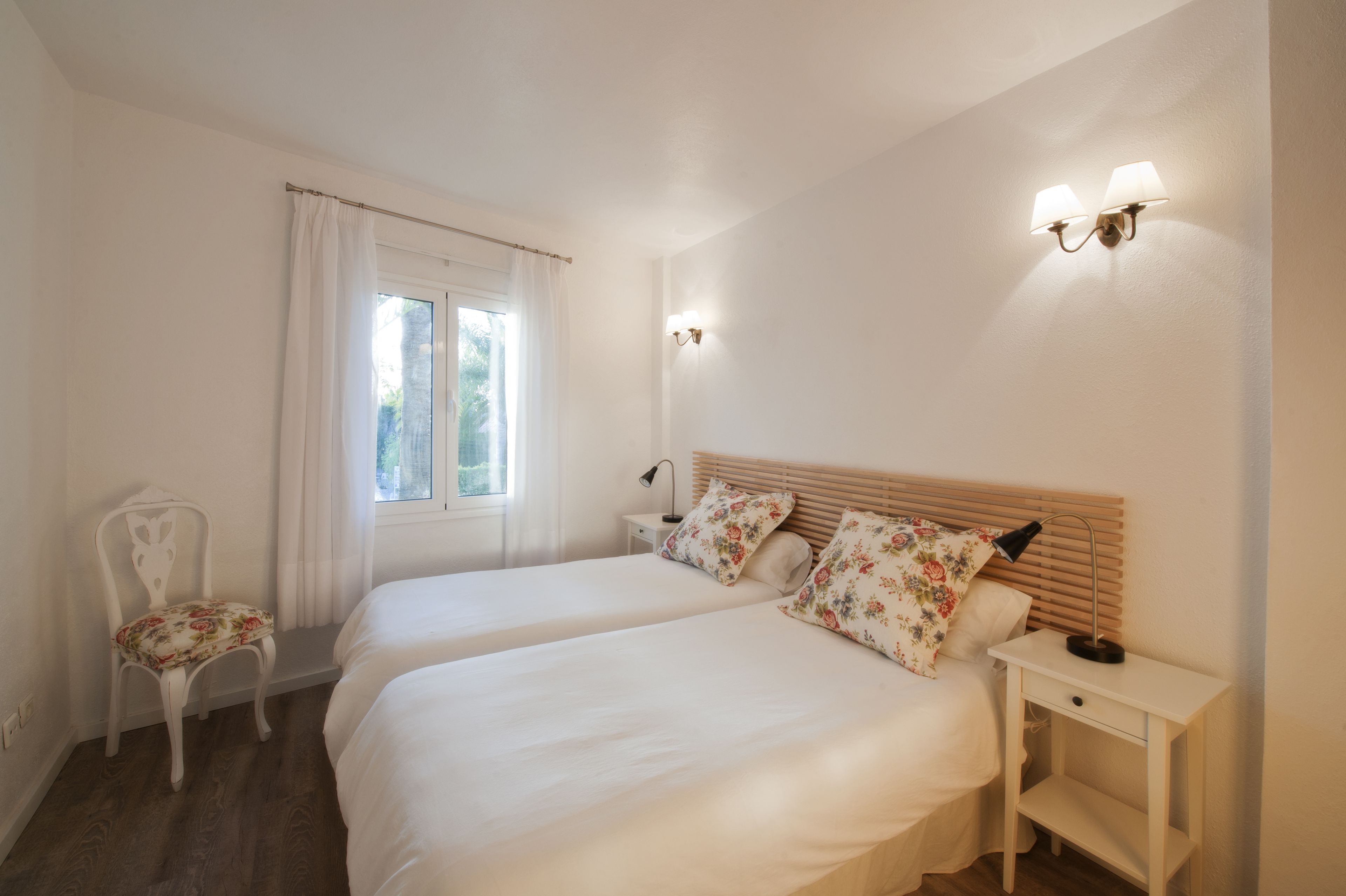 Une chambre avec deux lits, une chaise, une table de chevet et une fenêtre avec des rideaux.