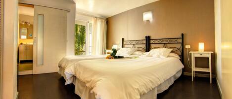 Una cama grande con ropa blanca, una mesita de noche con lámpara, y vistas a un baño con espejo y lavabo.