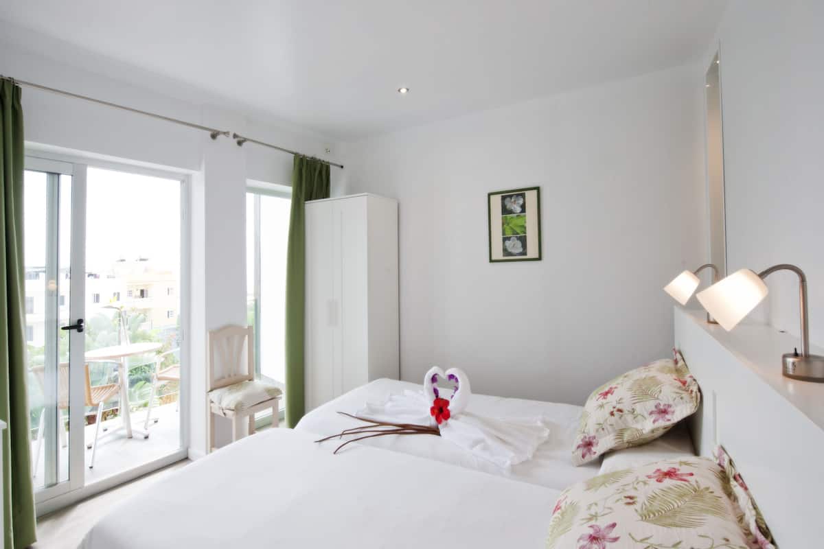 A hotel room with a bed, a chair, a wardrobe, a balcony with a table and chairs, and a picture on the wall.
