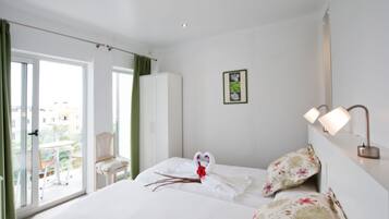 Habitación de hotel con cama, una silla, armario, balcón con mesa y sillas, y un cuadro en la pared.