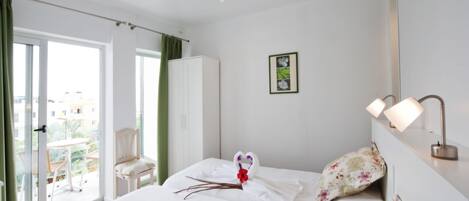 A hotel room with a bed, a chair, a wardrobe, a balcony with a table and chairs, and a picture on the wall.