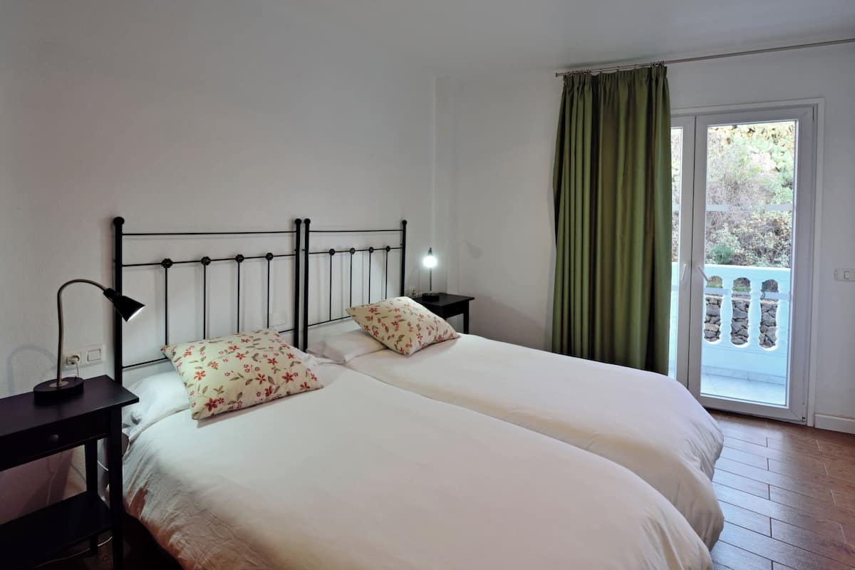 A double bed with a metal headboard, two bedside tables with lamps, and a view of a balcony through a sliding door.