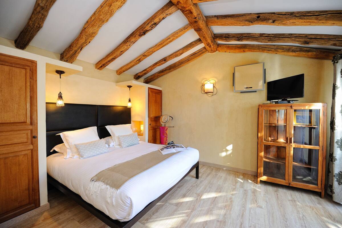 A bedroom with a wooden ceiling, a bed with white linens, a wooden cabinet, and a television on the wall.